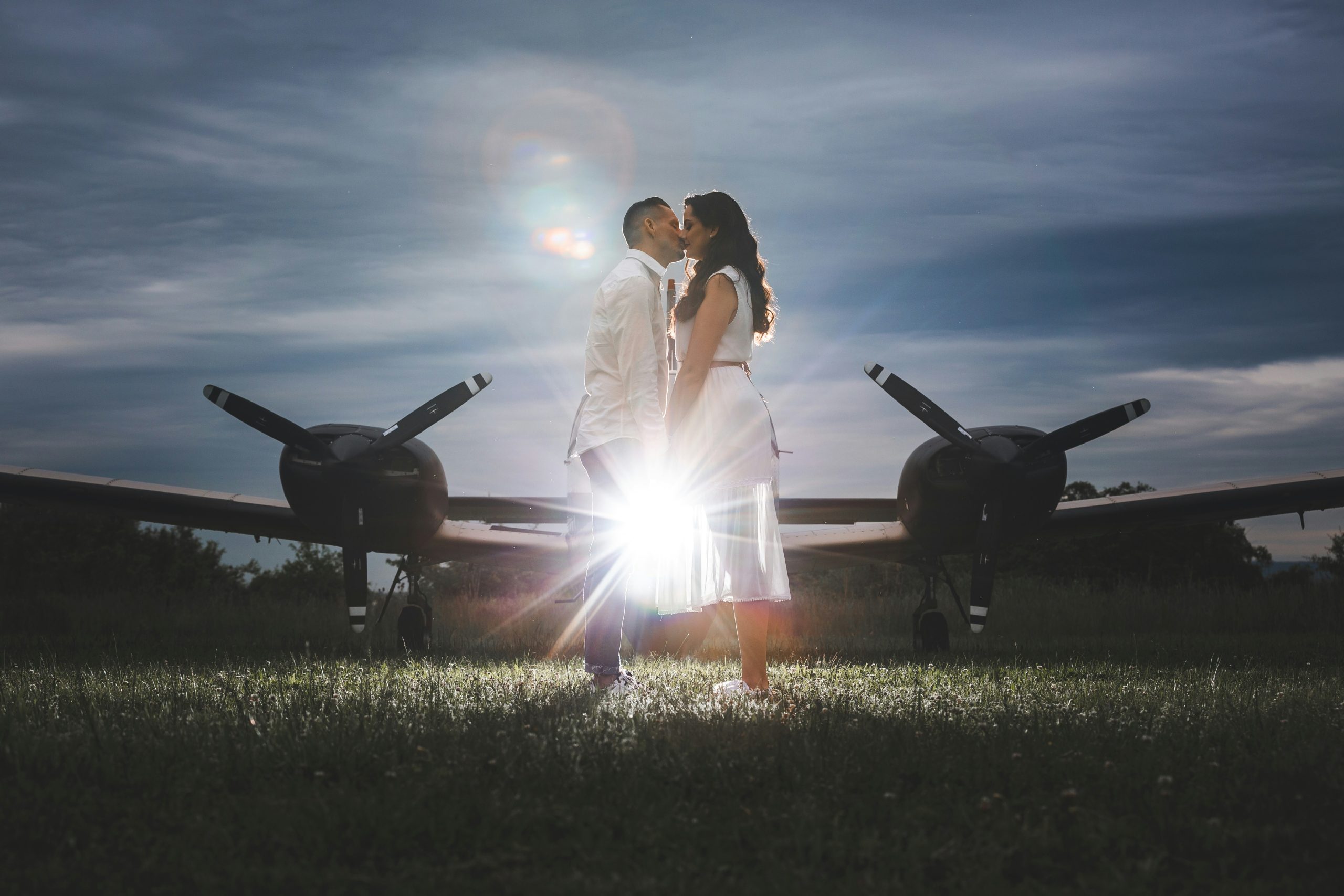 Man and his fiance close together, kissing, in front of a private plane.